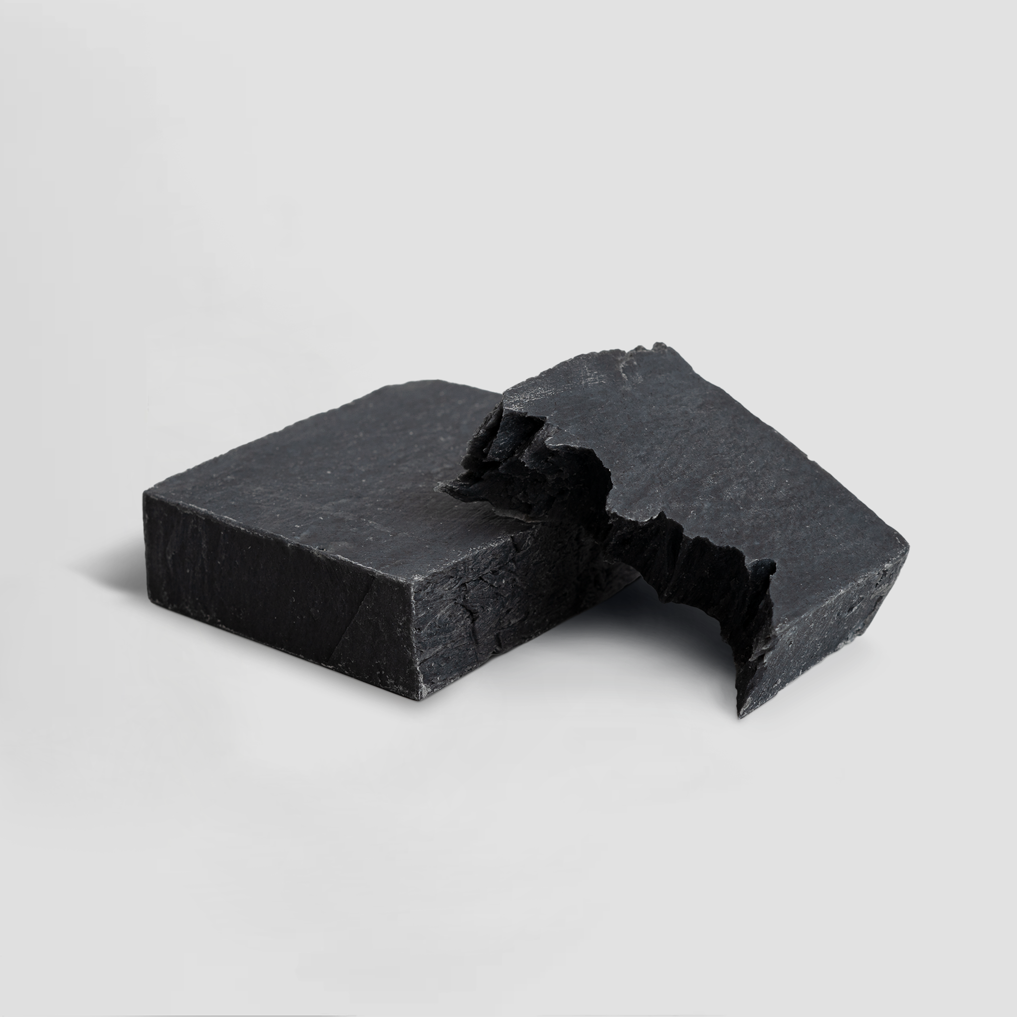 Two pieces of black soap on a light gray background