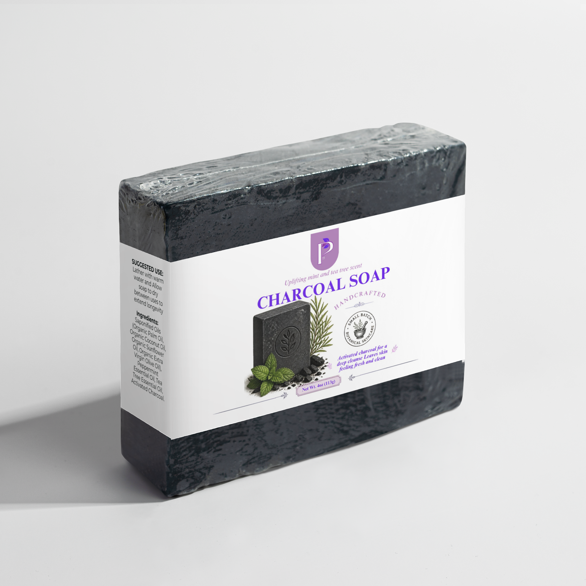 A wrapped bar of charcoal soap in a rectangular box with a white label, photographed on a clean light gray studio background. The label reads Charcoal Soap and shows a dark soap bar with mint leaves and botanical illustrations.