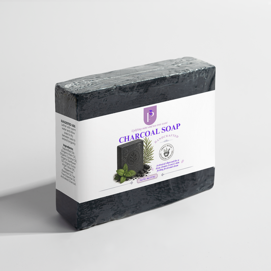 A wrapped bar of charcoal soap in a rectangular box with a white label, photographed on a clean light gray studio background. The label reads Charcoal Soap and shows a dark soap bar with mint leaves and botanical illustrations.