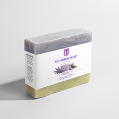 A bar of Slumber Soap by Apothecary, featuring a lavender-colored top half with visible botanical flecks, a yellow-green bottom half, and a white paper label wrapped around it. The label displays the brand name 'Apothecary' and the product name 'Calming Lavender & Herbal Sleep Soap'.