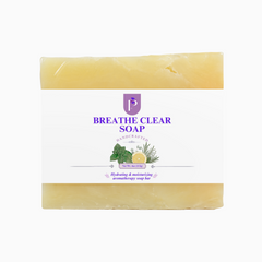 A rectangular bar of handcrafted soap with a white paper label, featuring a purple 'BREATHE CLEAR SOAP' logo and botanical illustrations. The soap itself is a pale yellow color, visible at the top and bottom edges of the label.