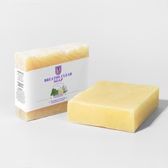 A bar of yellow soap shown next to its wrapped packaging. The soap bar is in the foreground, and the packaging box is behind it.