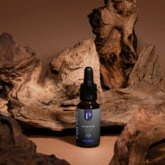 A small amber dropper bottle labeled 'FOR MEN P MAINTAIN Extreme Skin Oil' stands centered in front of rustic driftwood pieces on a warm brown surface.