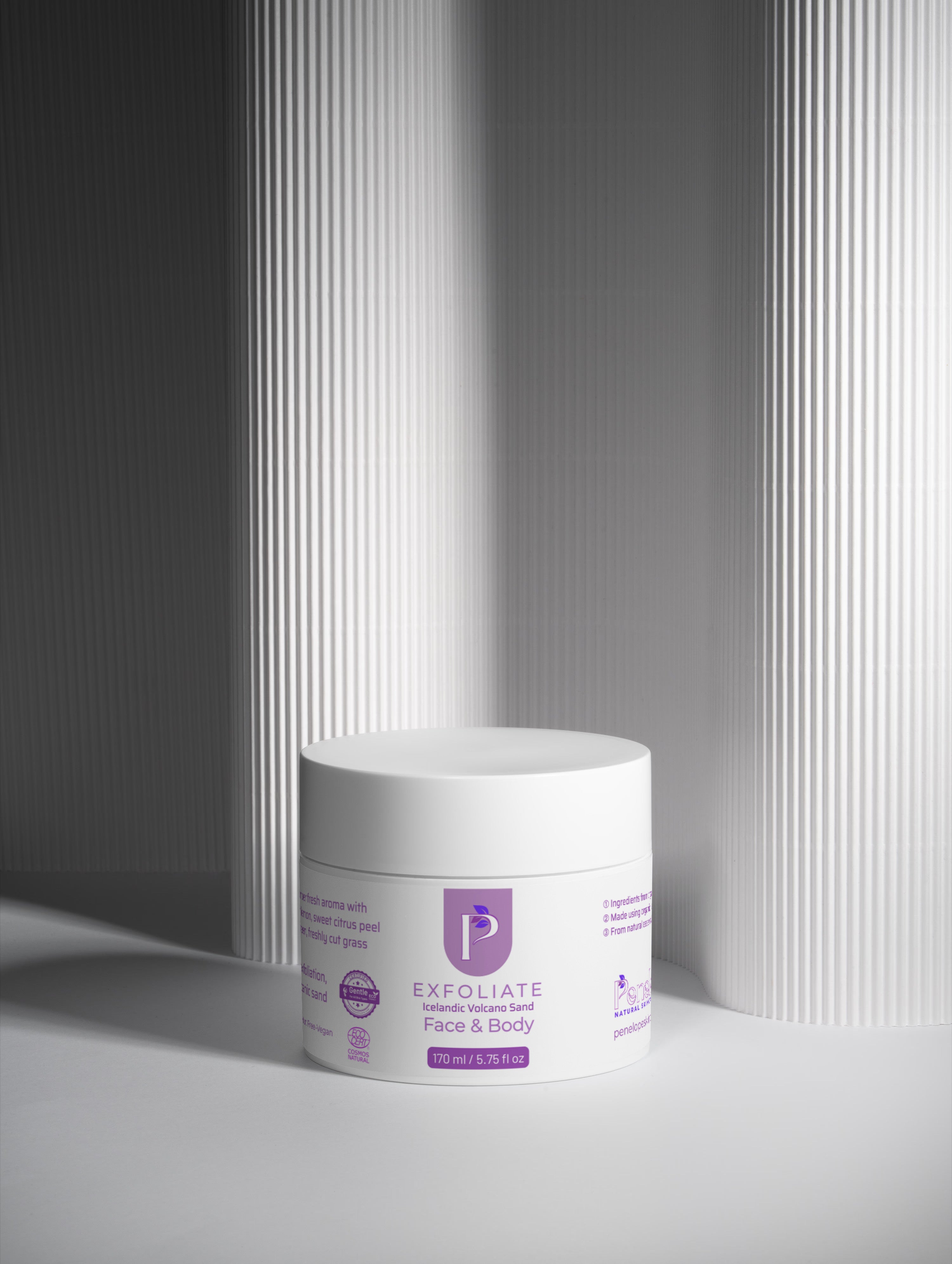 A white cosmetic jar labeled 'P Exfoliate Exfoliating Mask Face & Body' placed on a light gray surface with vertical ribbed panels in the background.