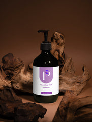 A dark amber pump bottle of hand and body wash with a white and purple label reading 'Hand & Body Wash Grapefruit' and a stylized 'P' logo, set against a warm brown background with decorative driftwood.