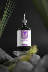 A pump bottle of Grapefruit Hand & Body Wash by 'p' (Purple Pillar) is displayed on a stack of gray stones with green grass against a dark background.