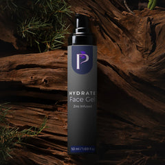 A 50 ml bottle of Hydrate Face Gel with Zinc Infused, featuring a dark gray body and black pump, set against a rustic background of weathered wood and pine needles.