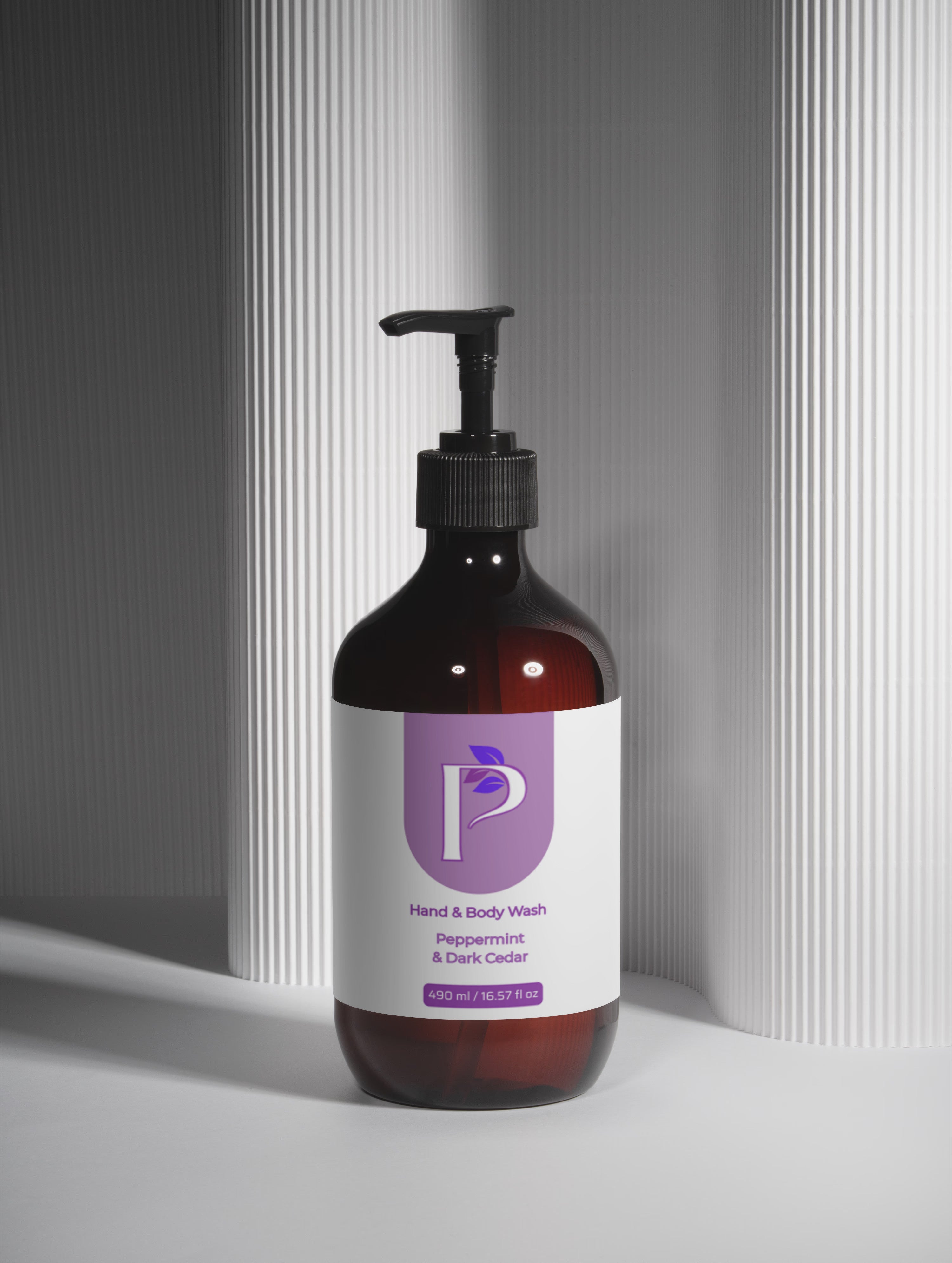 An amber glass pump bottle of hand and body wash with a black dispenser and a white label featuring a purple logo, set against a gray background with vertical ribbed panels.
